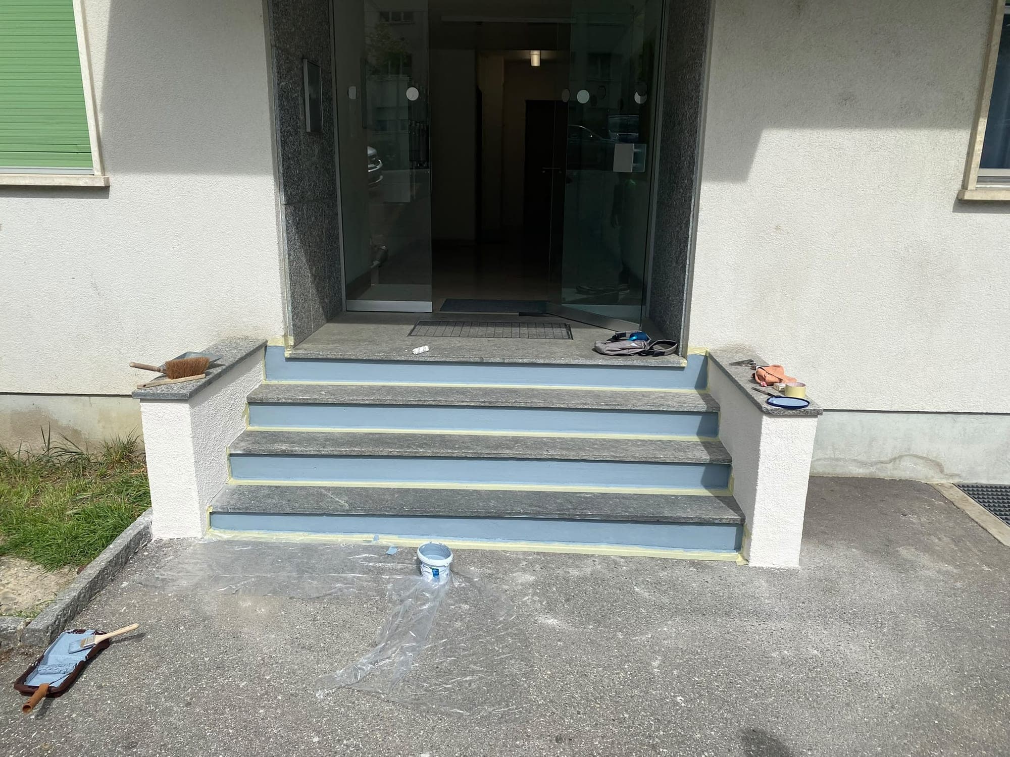 Même entrée d'immeuble en cours de travaux, contremarches fraîchement peintes et bâches au sol