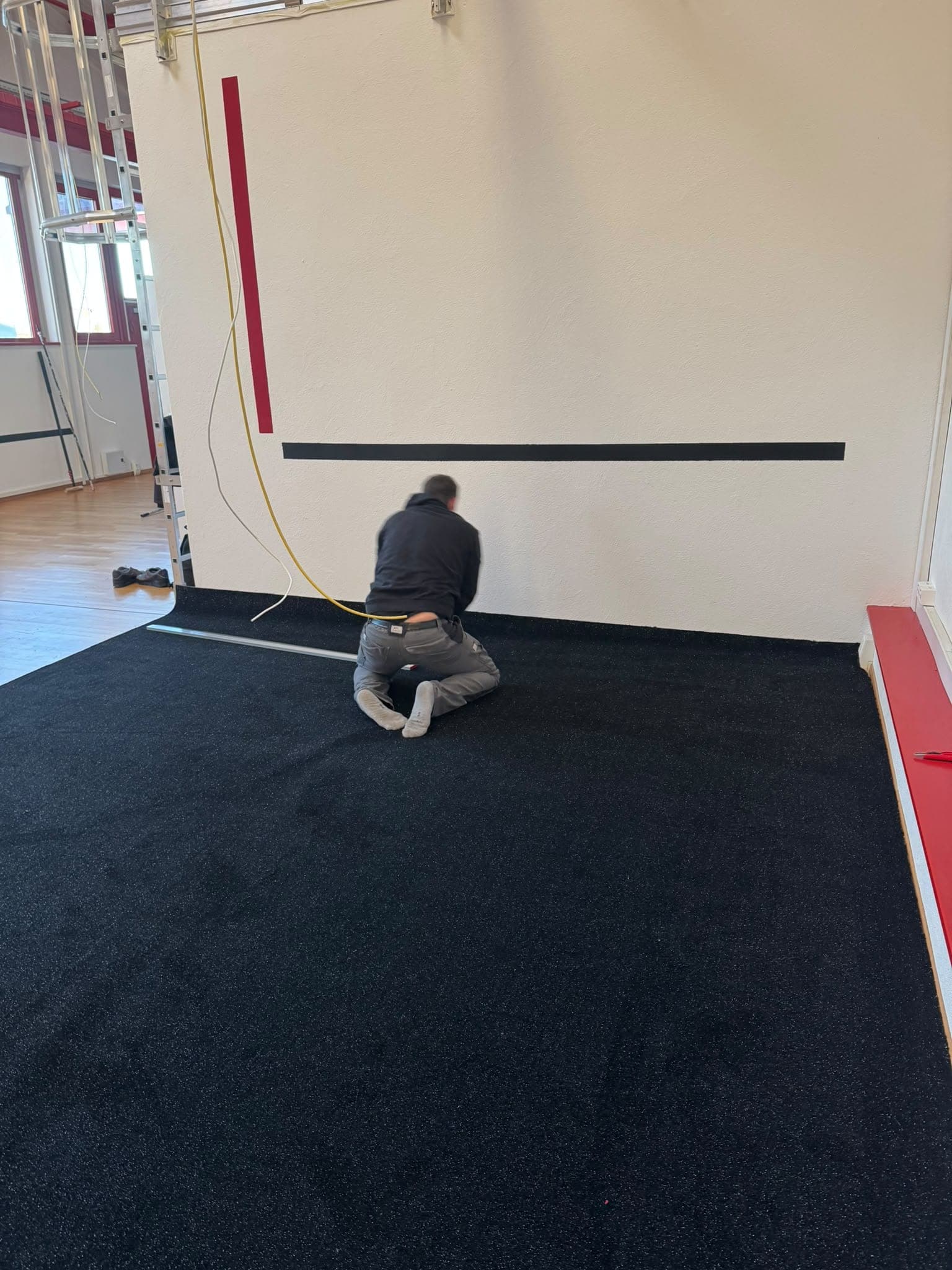Pose de la finition en pied de mur sur une moquette fraîchement déroulée