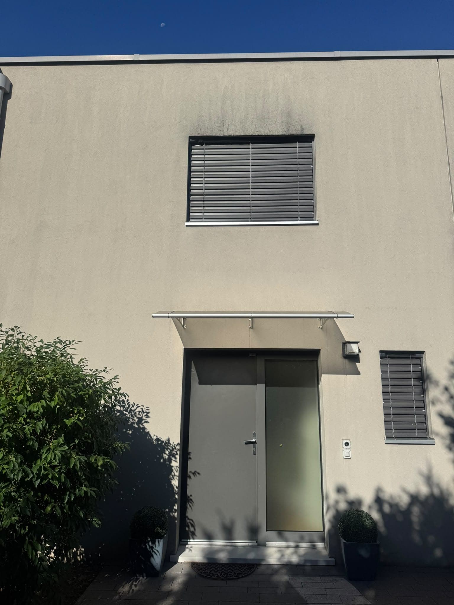 Entrée de villa dont le crépi est marqué d'une coulure sombre sous la fenêtre