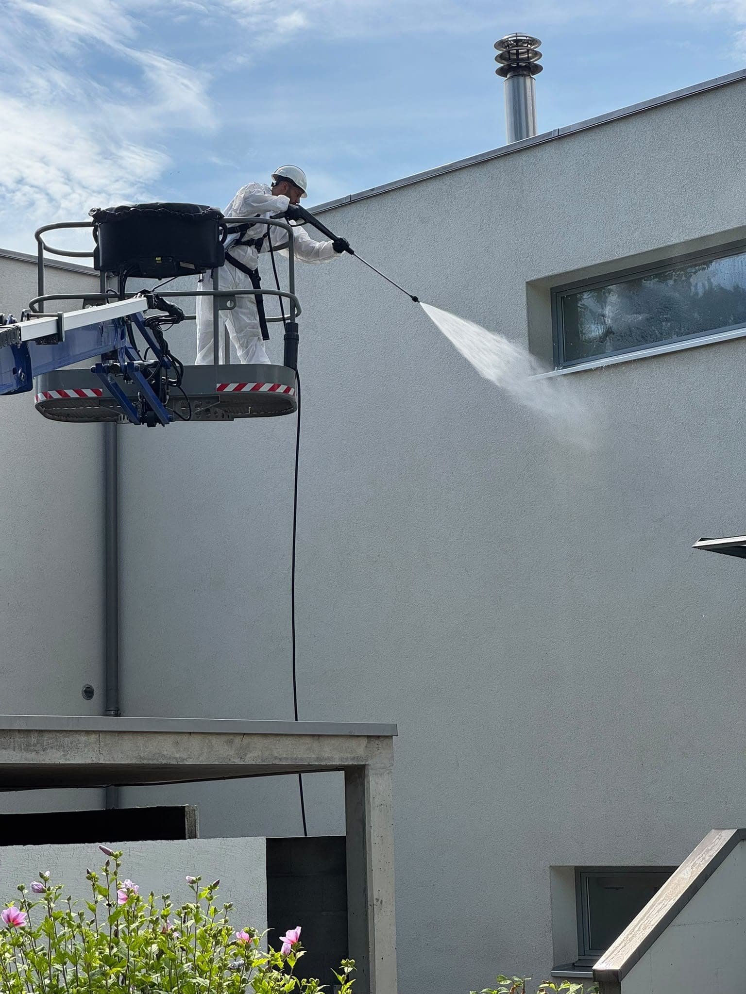 Jet de nettoyage projeté sur une façade grise depuis une nacelle élévatrice