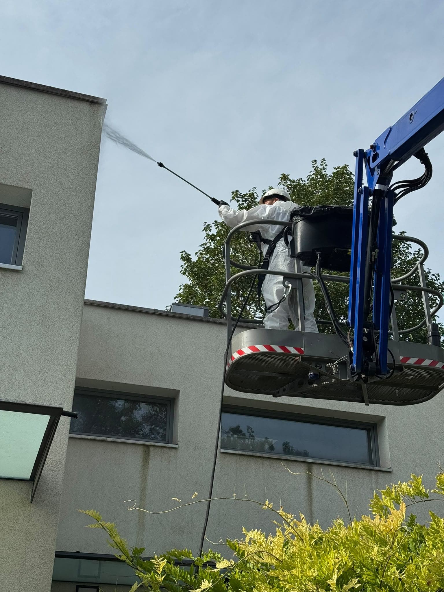 Opérateur en combinaison blanche et casque pulvérise un produit de traitement depuis une nacelle