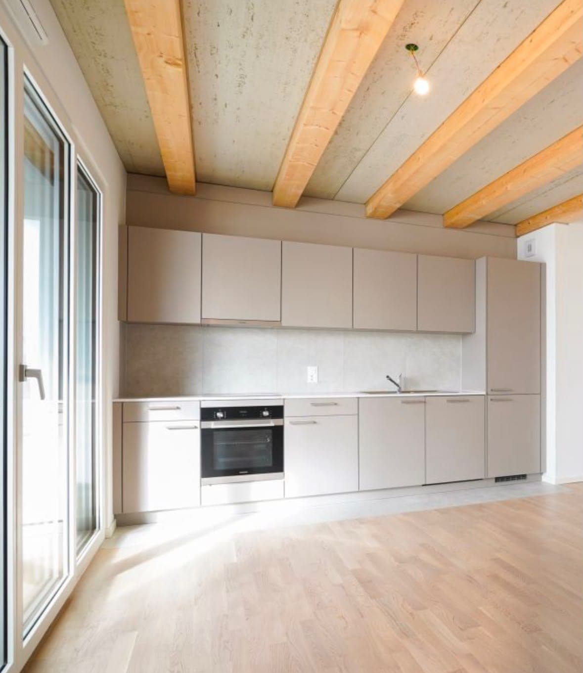 Cuisine neuve beige sous un plafond à poutres apparentes, parquet clair